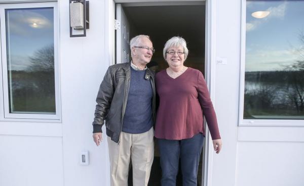 A happy older couple stands at the entrance to their house